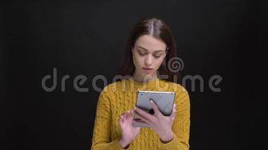 一幅长头发的黑发女孩穿着黄色毛衣，<strong>专心</strong>地用平板电脑和摄像机观看的肖像